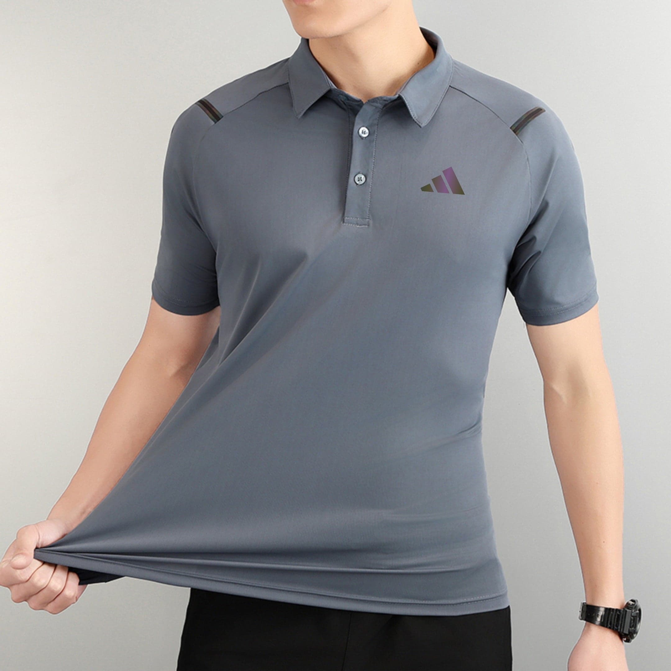 9dd6ba9b | AE JERSEY Person wearing a gray polo shirt with a small three-triangle logo on the left chest, pulling the hem downward.