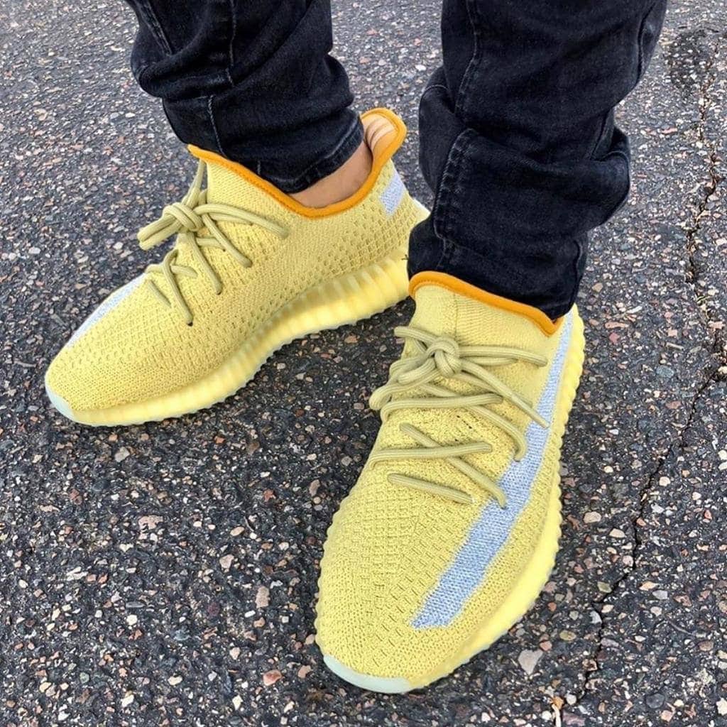 9f7a5406-5c99-4ec2-b593-16a5ce9ce4ca_add31471-f9de-4c18-a3b8-05d09178297b | AE JERSEY Yellow knit sneakers with pale laces on a person standing on asphalt in dark jeans (close-up).