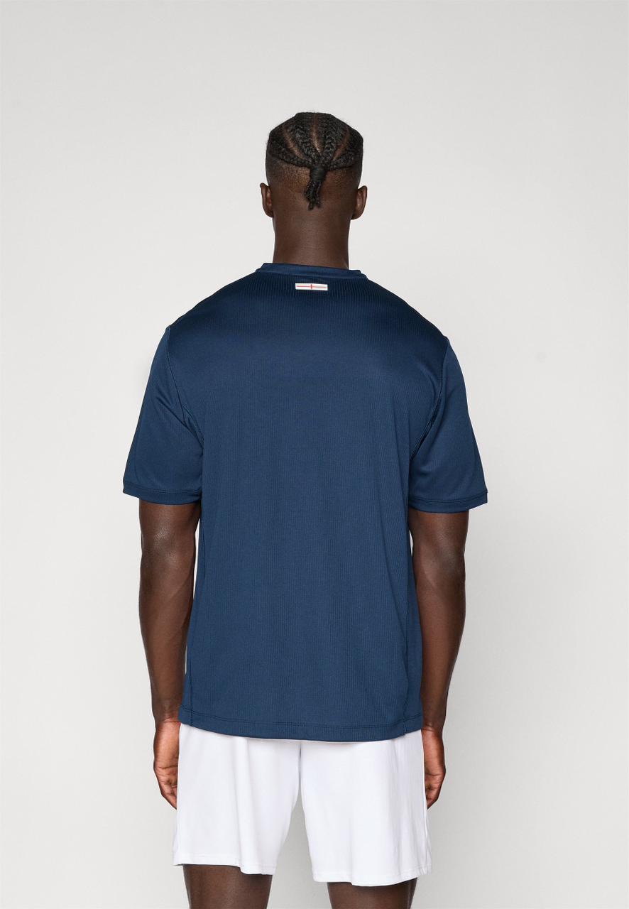 9fc9e2ac-feda-4ec0-b7ce-7cbe49b33561 | AE JERSEY Back view of a man wearing a navy T-shirt and white shorts, with braided cornrow hairstyle, standing against a light wall.