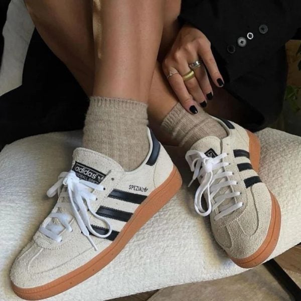 Beige Adidas Spezial sneakers with white laces and black stripes resting on a light cushion, beige socks visible.