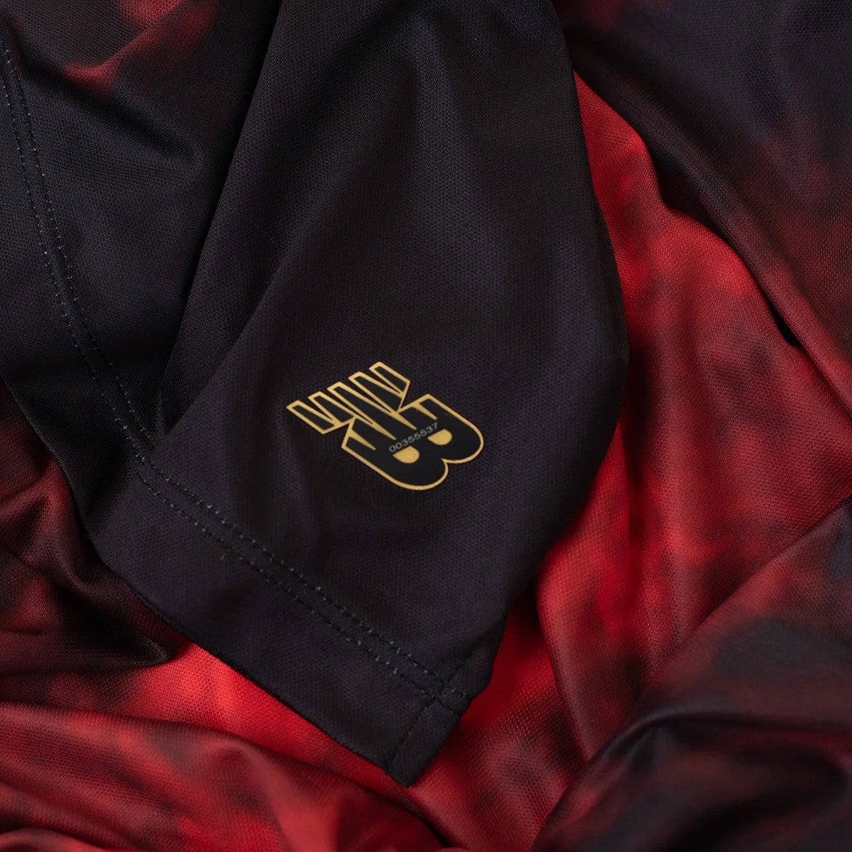 CIpPttJ6gobvgEE | AE JERSEY Close-up of black fabric with red lining and a small gold crest near a seam.