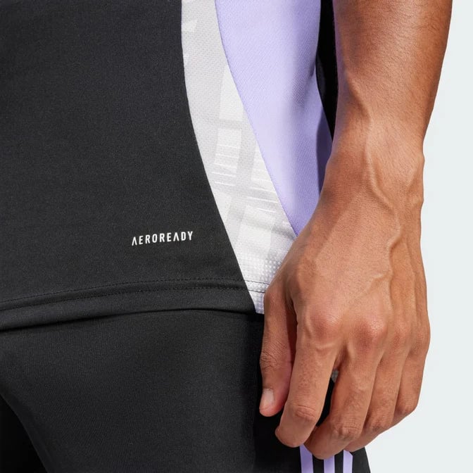 Camiseta_Entrenamiento_Colo-Colo_5_672x672_a3ec355c-cc84-4bc0-99c0-17b9aec56c1d | AE JERSEY Close-up of a person's hand by black athletic shorts with a white 'AEROREADY' logo and a purple panel on the jersey.