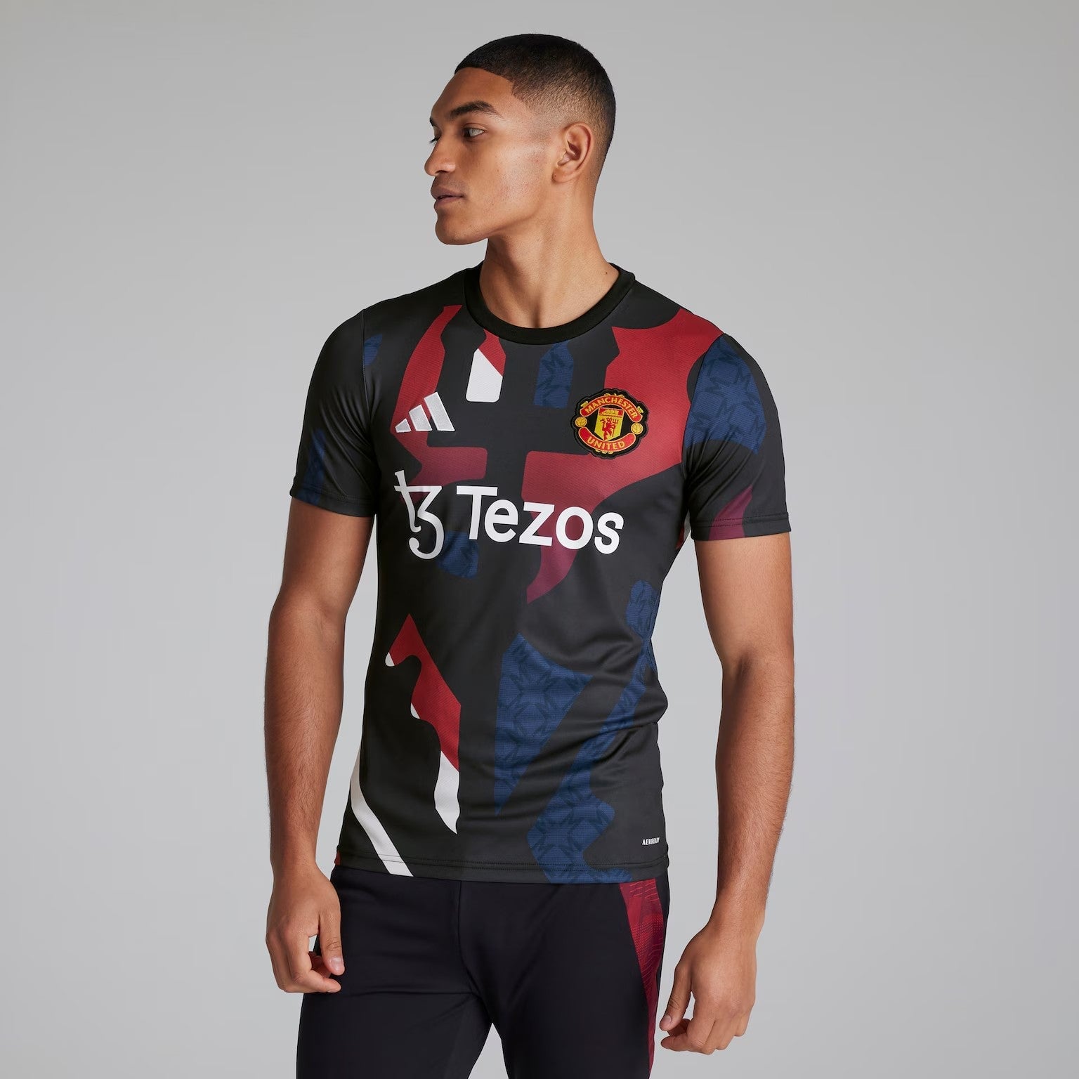 CtPGePzYm4TB886 | AE JERSEY Man wearing a black Manchester United jersey with red and blue geometric pattern and Tezos sponsor, looking to the left.