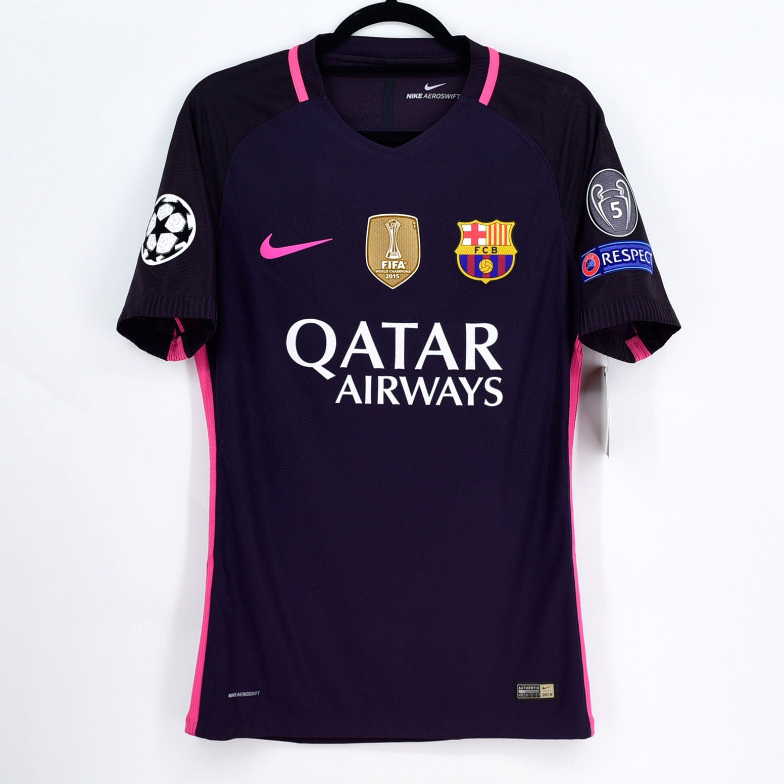 DSC2439 | AE JERSEY Dark blue FC Barcelona soccer jersey with pink accents on a hanger, featuring Qatar Airways sponsor text, Nike swoosh, Barca crest, and UEFA/Champions League patches on the sleeves.
