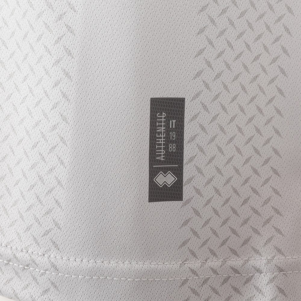 DvQM9pOQcaghLYY_ded72ace-6a8a-4e4d-bd82-4670ac890cc3 | AE JERSEY Close-up of light gray textured fabric with a small black tag featuring vertical text and a diamond-shaped logo.