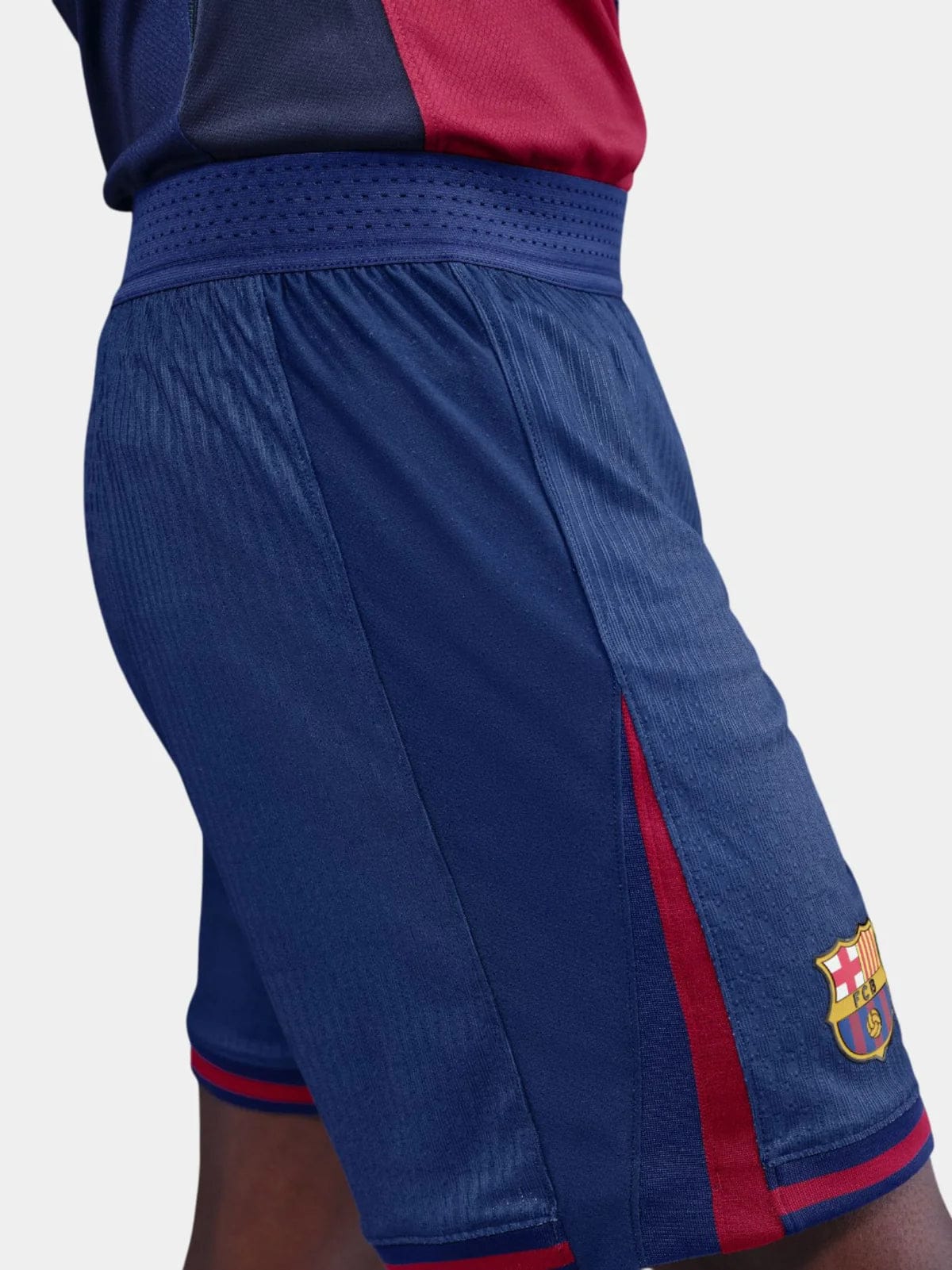 GE | AE JERSEY Side view of blue FC Barcelona shorts with a red stripe down the leg and the club crest near the hem on light fabric mix