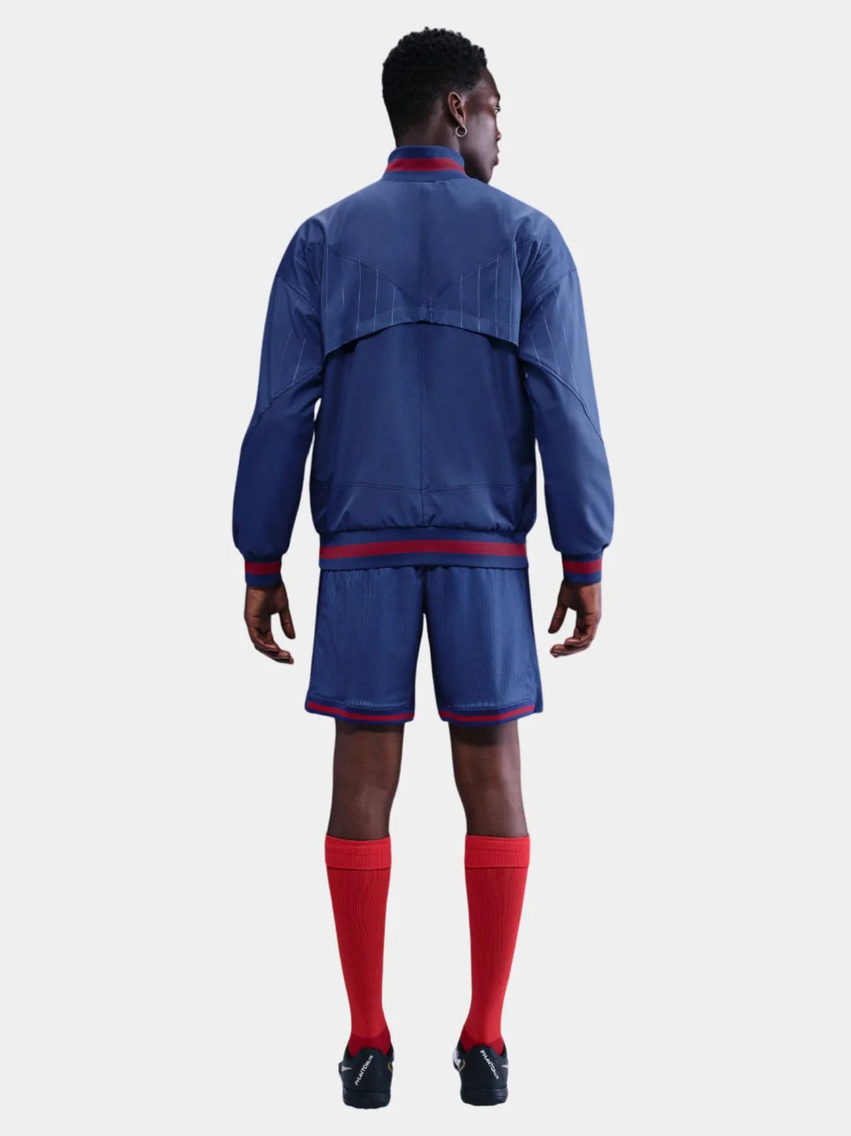 GY | AE JERSEY Back view of a person in a blue athletic jacket and matching shorts with red trim and red socks from behind.