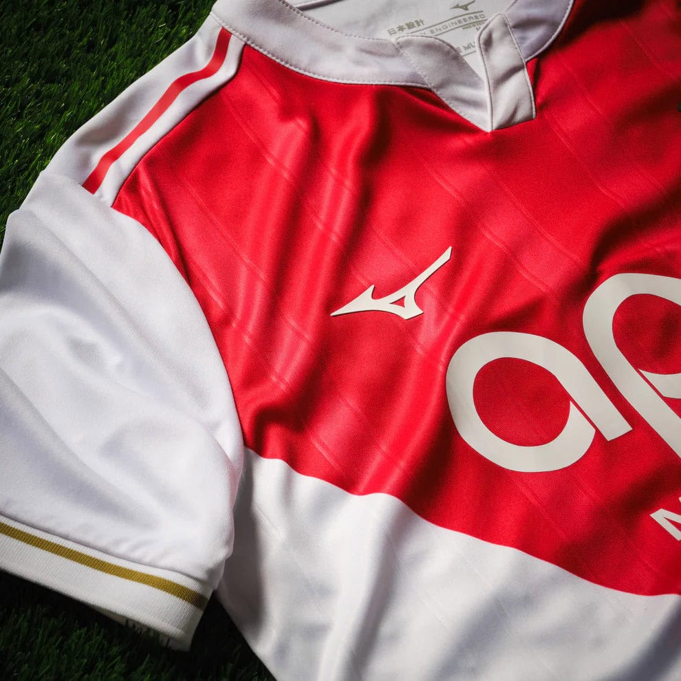Home_Jersey_Monaco_M_Tango_Red_P2GACX75_59_Close2 | AE JERSEY Red and white sports jersey laid on green grass, showing a white Mizuno logo and large partial number on the front.