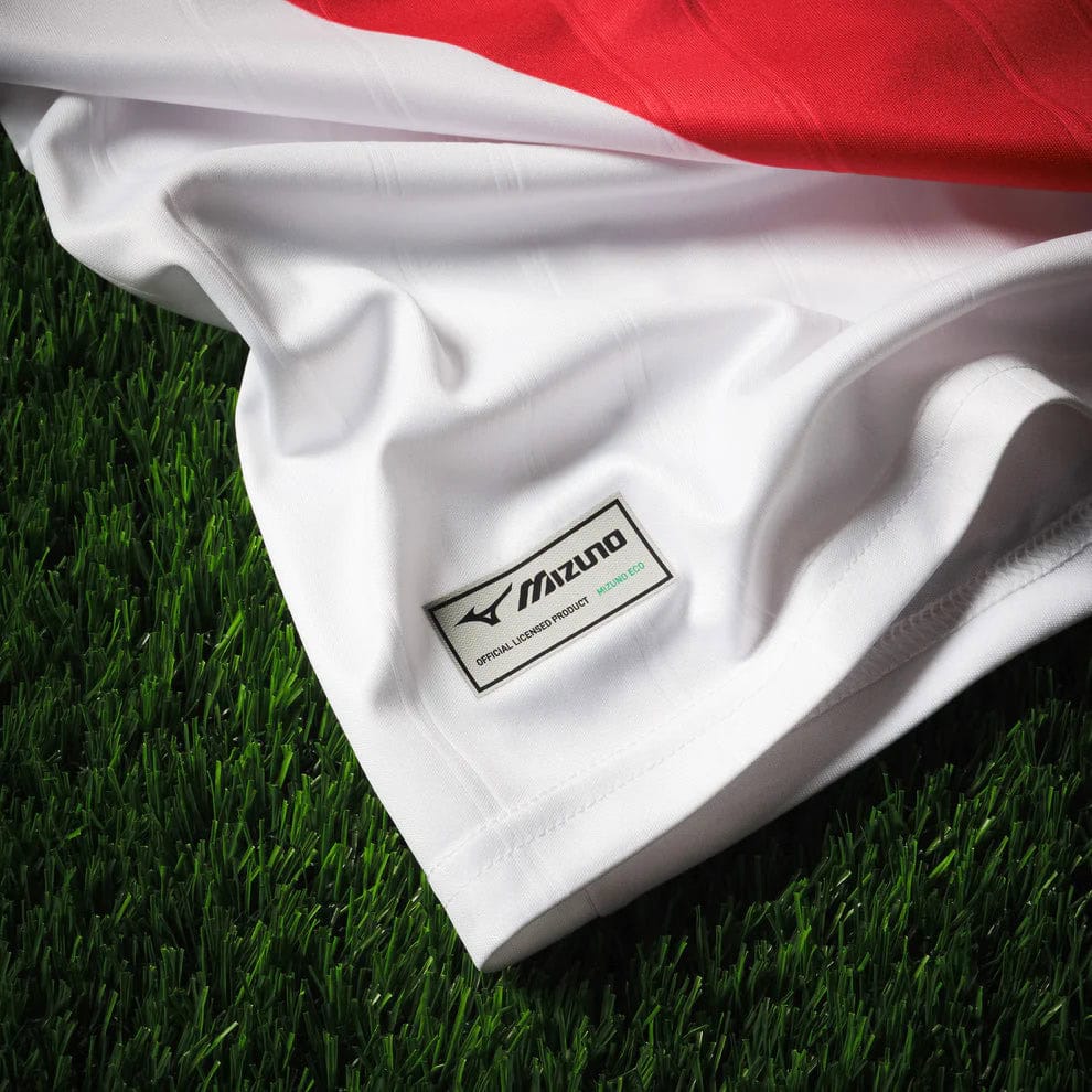 Home_Jersey_Monaco_M_Tango_Red_P2GACX75_59_Close3 | AE JERSEY White Mizuno jersey on artificial grass with a small official licensed product tag visible on the fabric edge.