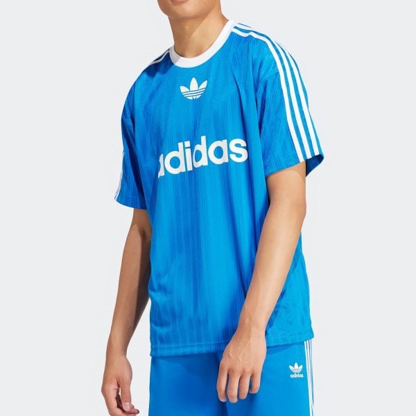 Close-up of a person wearing a bright blue Adidas jersey with white trefoil logo and sleeve stripes, shown from the chest down to the waist.