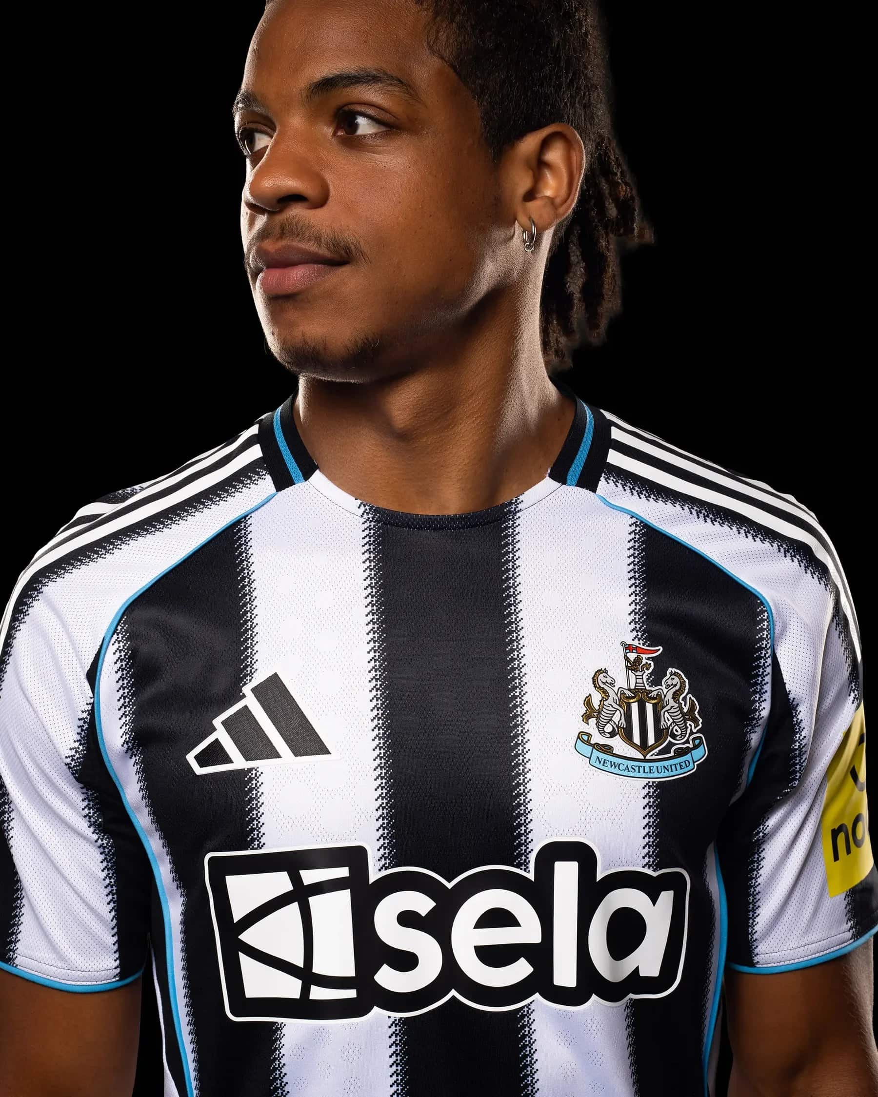 JI7391_MOD_25v2 | AE JERSEY Close-up of a person wearing a black-and-white striped Newcastle United football jersey with crest visible on the chest against a black background.
