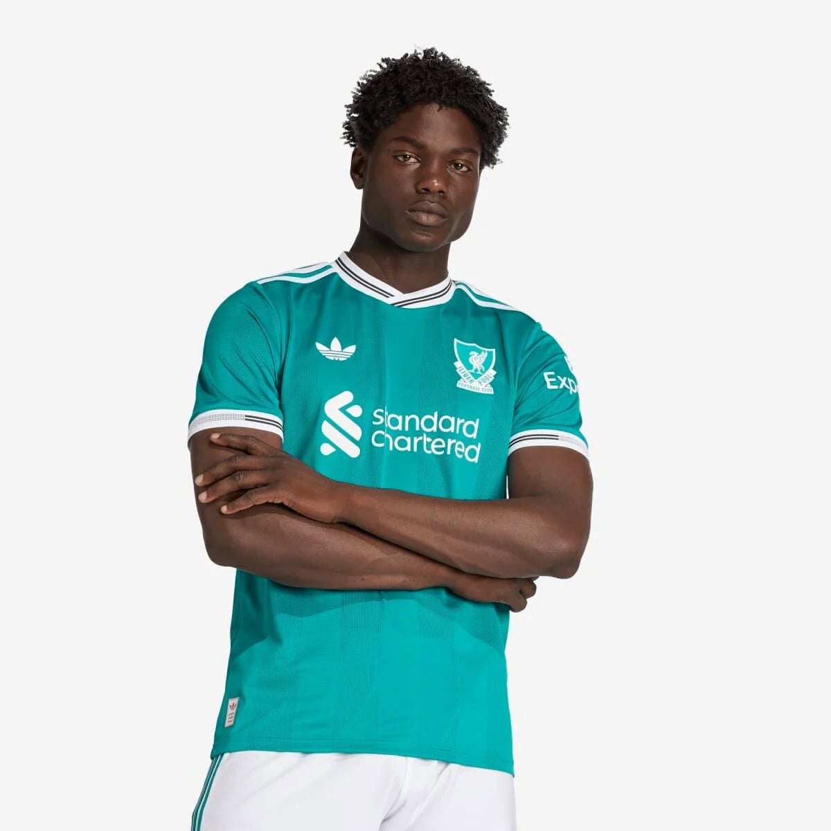 JV6427_3_APPAREL_OnModel_StandardView_custom_1-lowres | AE JERSEY Man wearing a teal Liverpool FC jersey with the Standard Chartered sponsor, arms crossed, looking at the camera.