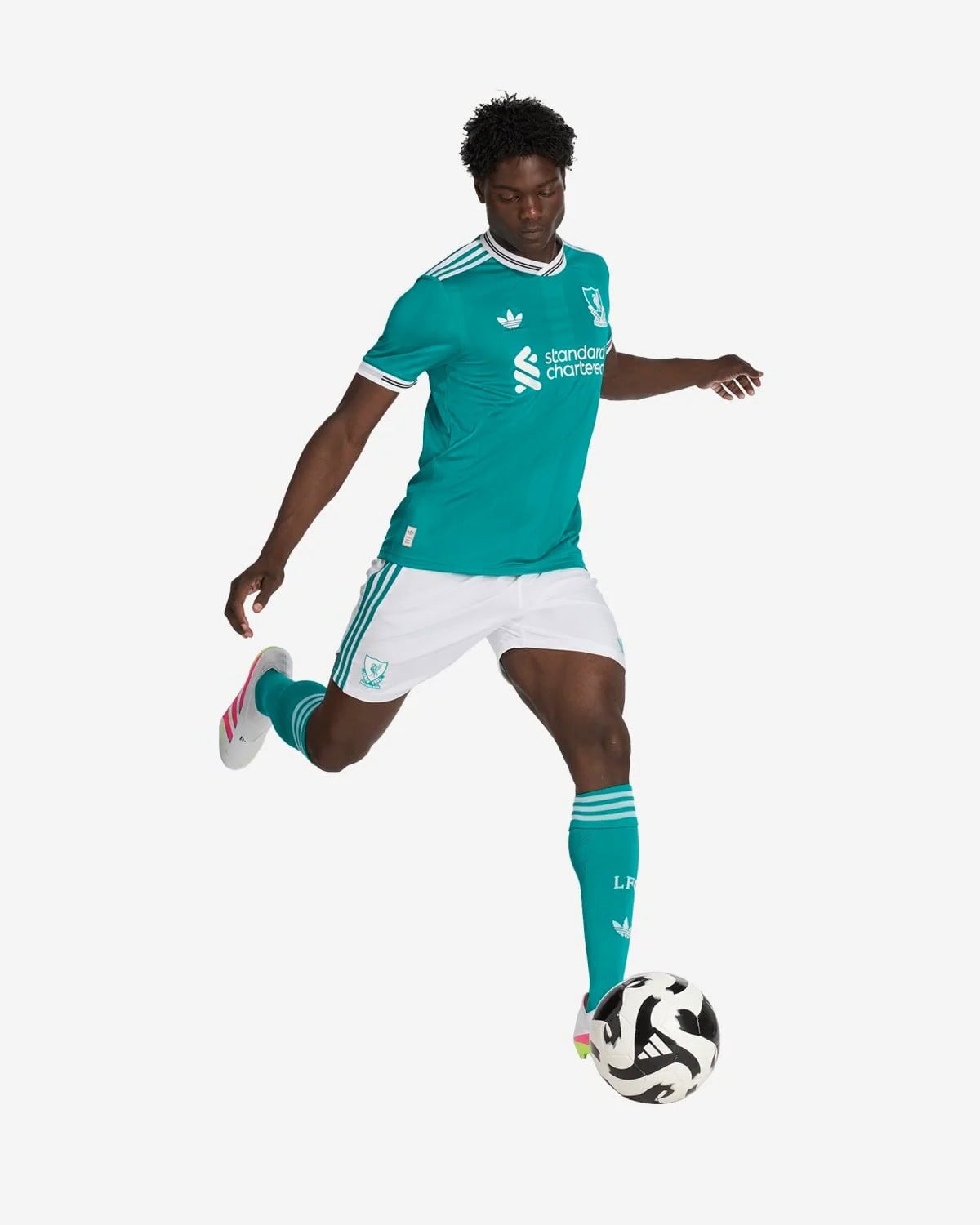 JV6427_5_APPAREL_OnModel_WalkingView_custom_1-lowres | AE JERSEY Soccer player in teal away kit with white shorts kicking a soccer ball.