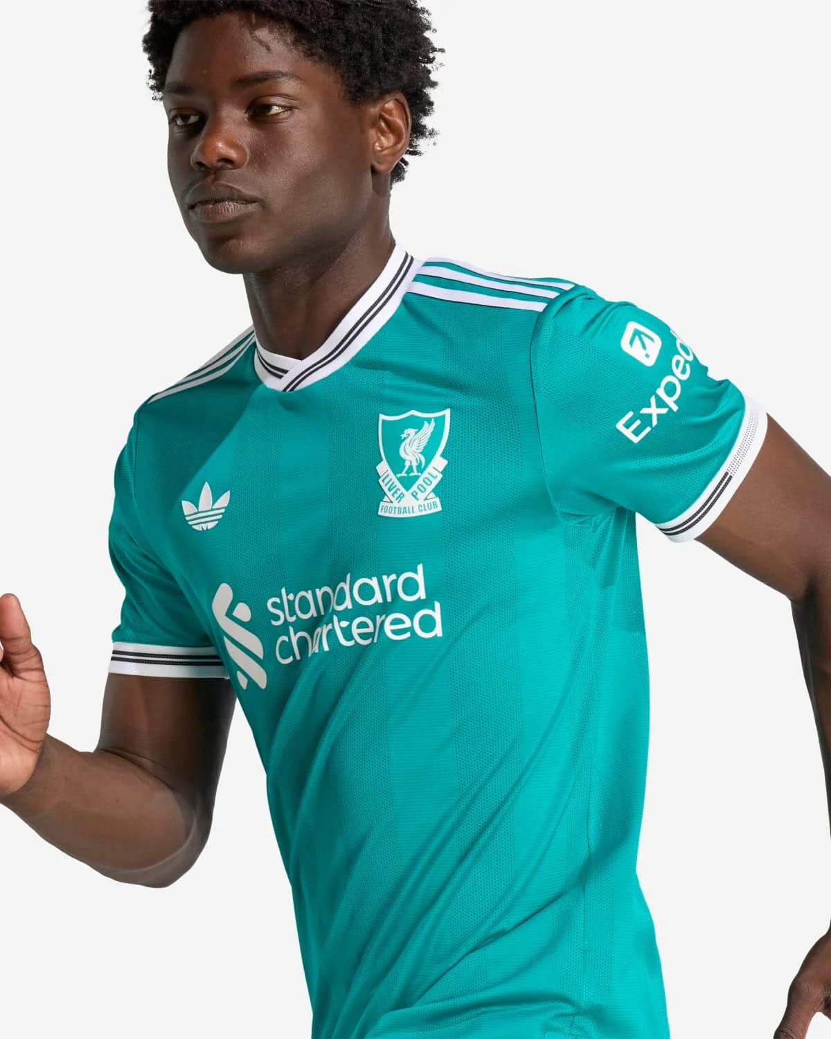 JV6427_8_APPAREL_OnModel_DetailView2_custom_1-lowres | AE JERSEY Athlete wearing a teal Liverpool FC football jersey with the Standard Chartered sponsor and crest visible on the chest.