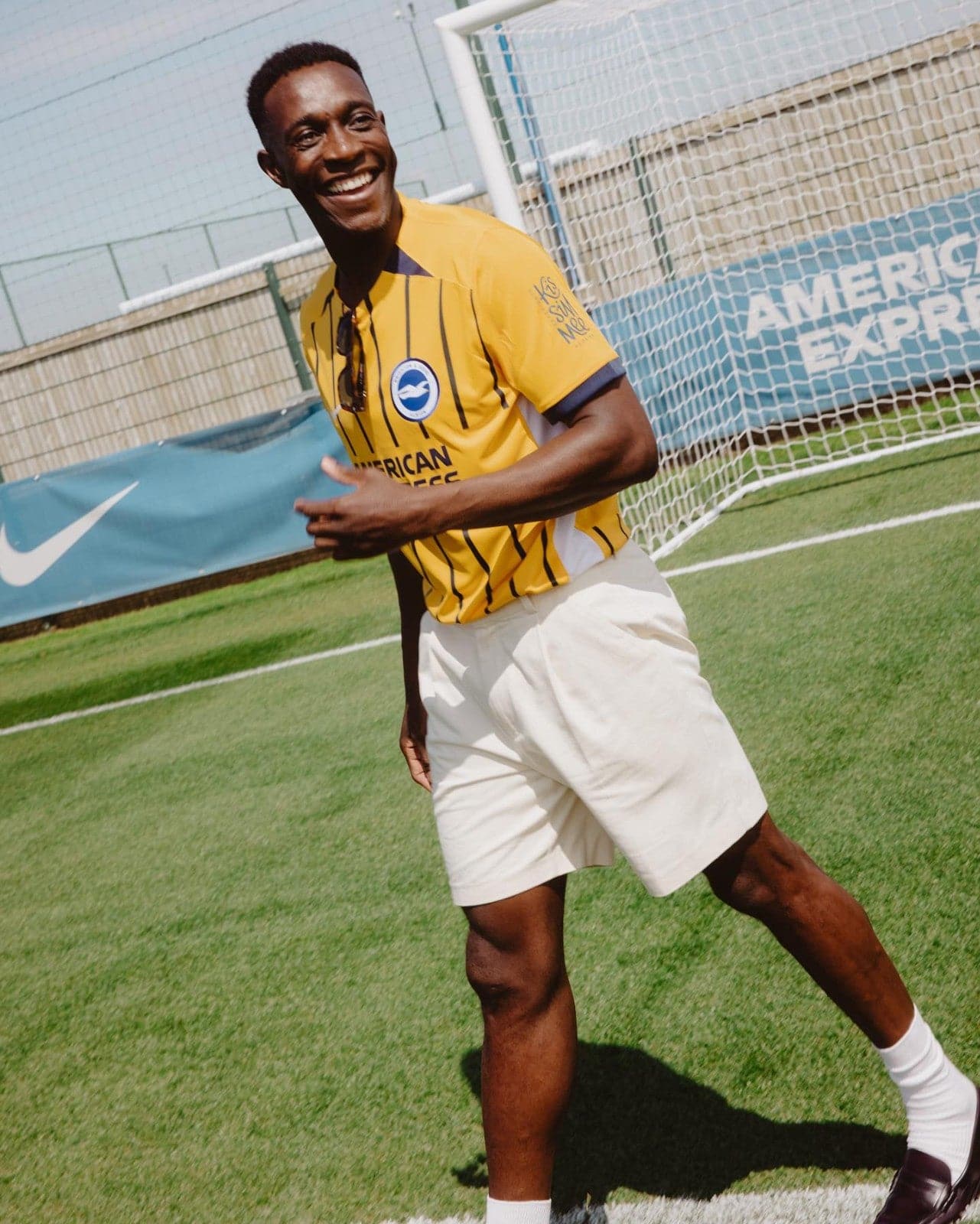 NqYSkXjGiTnQpPq | AE JERSEY Smiling man in a yellow striped soccer jersey on a sunny field, near a goal net.