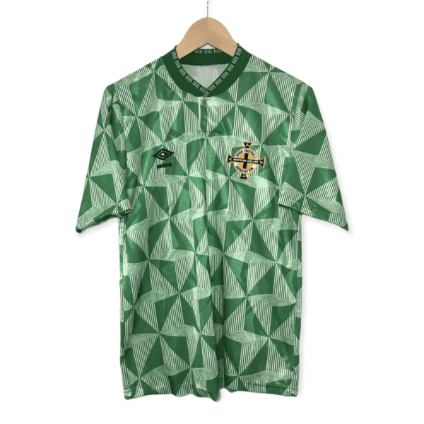 Green geometric football jersey hanging on a wooden hanger, featuring the Northern Ireland Football Association crest and Umbro logo on the chest.