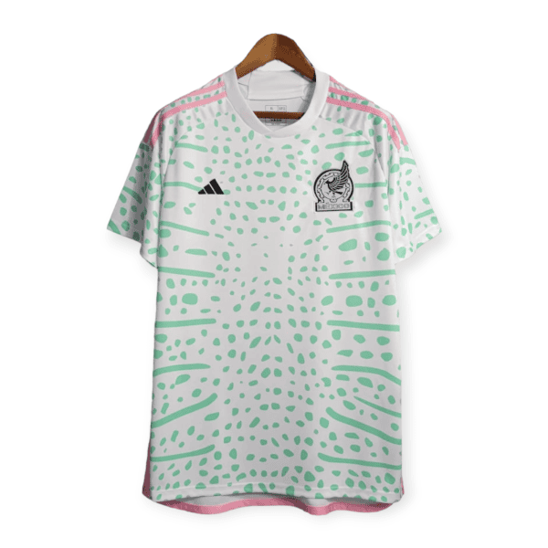 White Adidas jersey with green dot pattern, pink shoulder stripes, and Mexico crest on the chest, hanging on a wooden hanger.