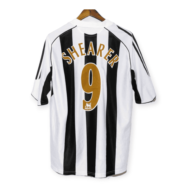 Back view of a black-and-white striped soccer jersey on a wooden hanger, with the name 'SHEARER' and number '9' in gold letters on the back.
