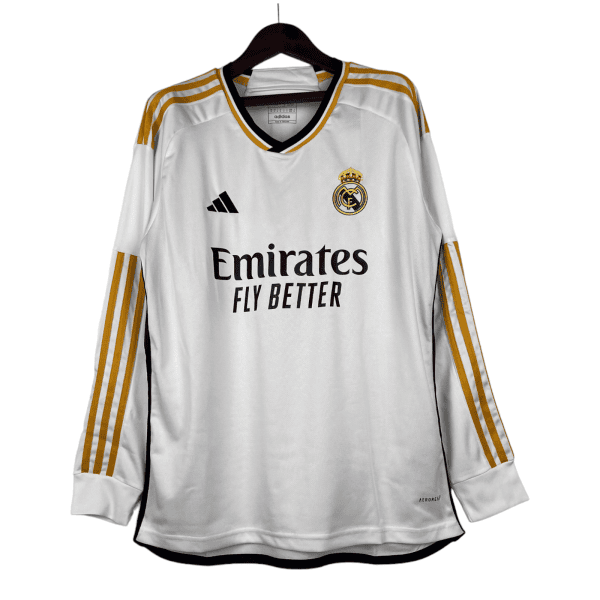 White Real Madrid football jersey on a hanger, with gold-striped sleeves, crest, Adidas logo, and Emirates Fly Better sponsor text.
