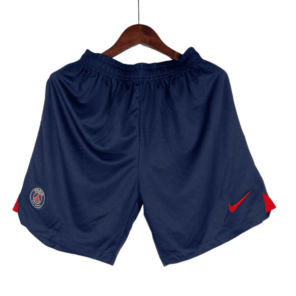 Navy athletic shorts on a wooden hanger with PSG crest on the left thigh and a red Nike swoosh.