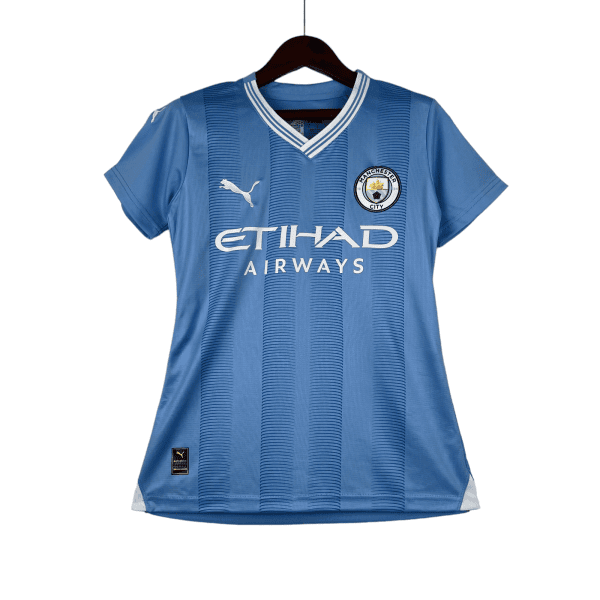 Blue Manchester City football jersey on a wooden hanger, showing the club crest, Puma logo, and Etihad Airways sponsor.