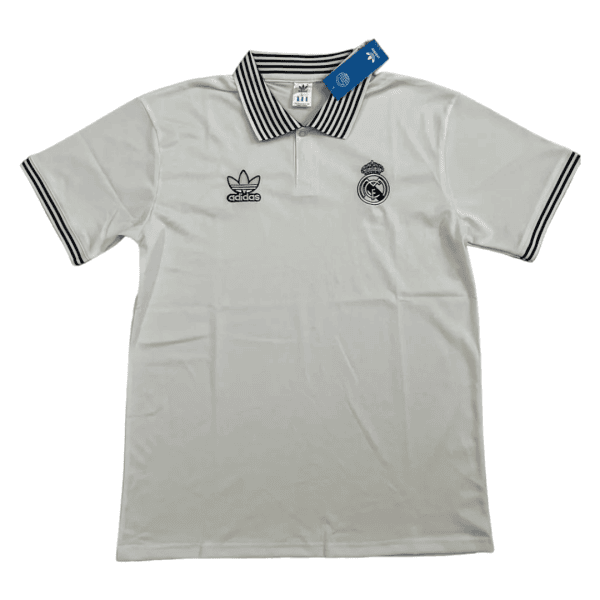 White polo shirt with Real Madrid crest and Adidas logo on the chest, black striped collar and sleeve cuffs, tag attached