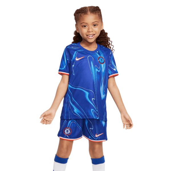 Smiling young girl in a Chelsea FC blue soccer jersey and shorts with white socks and orange trim.
