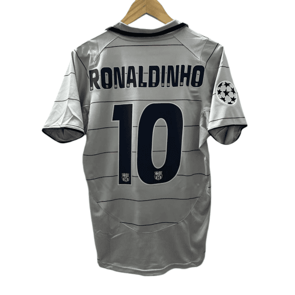 Gray soccer jersey hung on a wooden hanger, back shows 'RONALDINHO' and number 10 with a Champions League badge on the sleeve.
