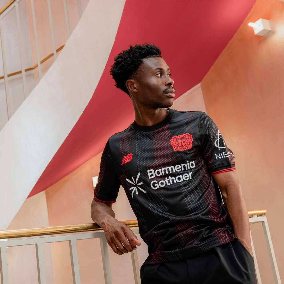 Soccer player in a black and red team jersey leaning on a railing in a colorful indoor stairwell, looking to the right.