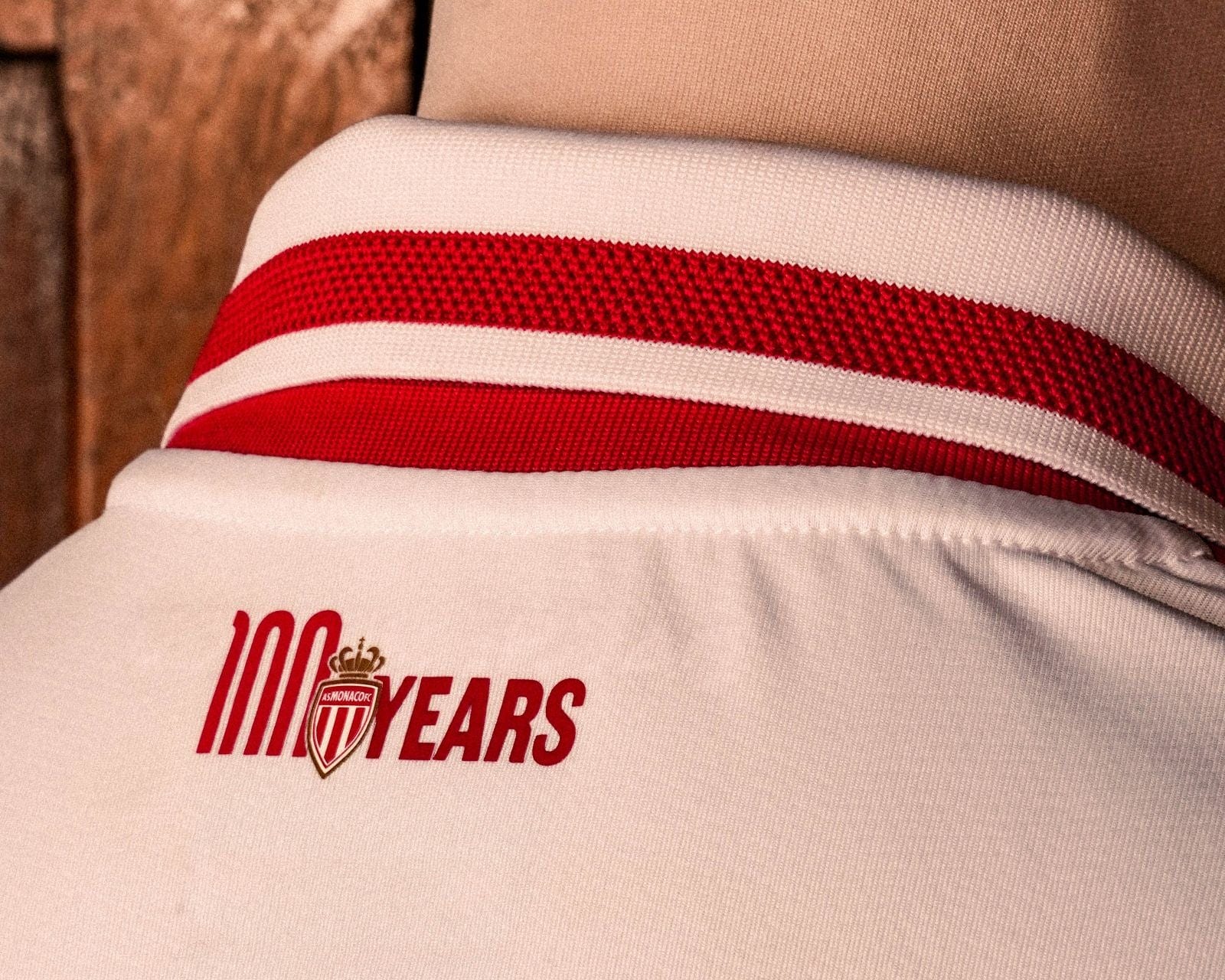 Pxmf1C1mSLScefo | AE JERSEY Close-up of white fabric with red stripe and a '100 YEARS' graphic and club crest