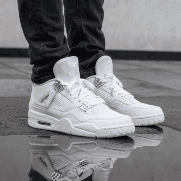 Pair of white sneakers with black jeans standing on wet pavement, their reflection visible in a puddle.