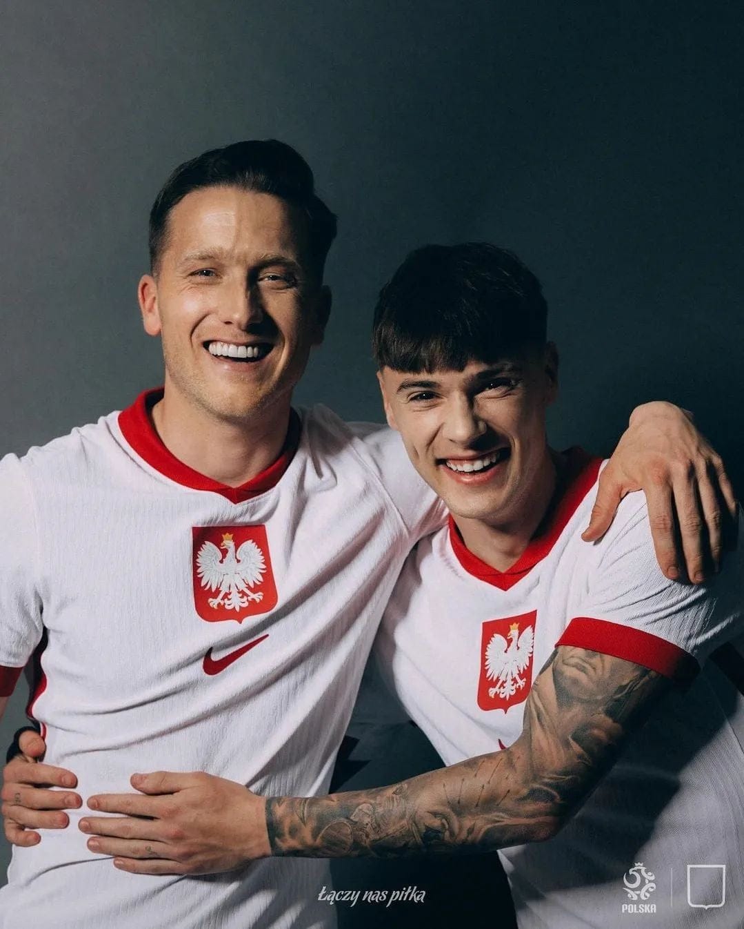 QUjAAoTMImF6MLY | AE JERSEY Two men in Poland national soccer jerseys smile with arms around each other in a friendly pose.
