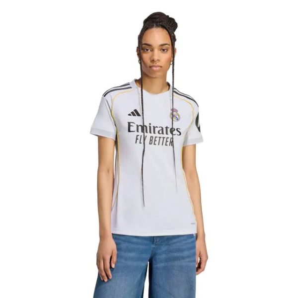 Woman modeling a light gray Real Madrid soccer jersey with Emirates Fly Better sponsor text, facing forward.
