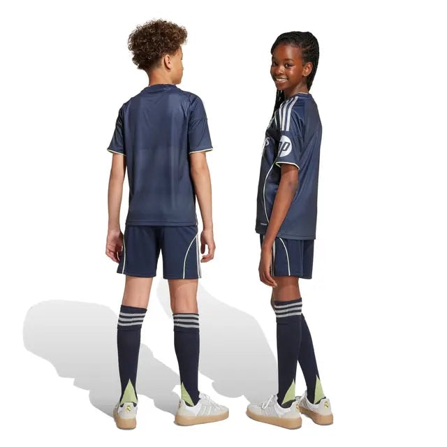 RMCFYO0095_11 | AE JERSEY Two children in matching navy sports uniforms stand back-to-back; the girl faces slightly toward the camera with a smile while the boy faces away. They wear navy jerseys, shorts, long socks, and light-colored sneakers.