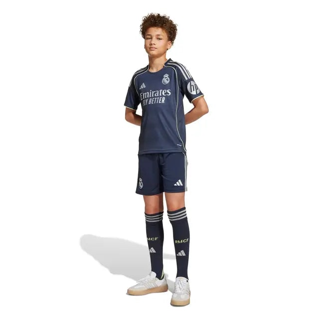 RMCFYO0095_6 | AE JERSEY Boy wearing a dark Real Madrid soccer jersey with matching shorts and long socks, standing with hands behind back and white sneakers.