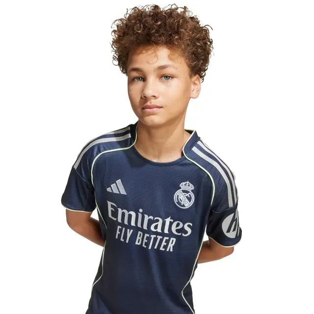 RMCFYO0095_9 | AE JERSEY Young boy with curly hair wearing a navy Real Madrid football jersey featuring the Emirates Fly Better sponsor logo on the front.
