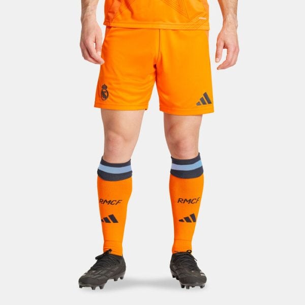 Lower-body view of a footballer in bright orange shorts and matching orange socks with RMCF letters and Adidas logos, wearing dark football boots.