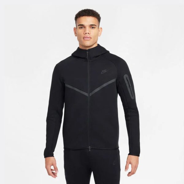 Front view of a man wearing a black Nike zip-up hoodie with a high collar and reflective chevron design across the chest and a zip pocket on the left sleeve.