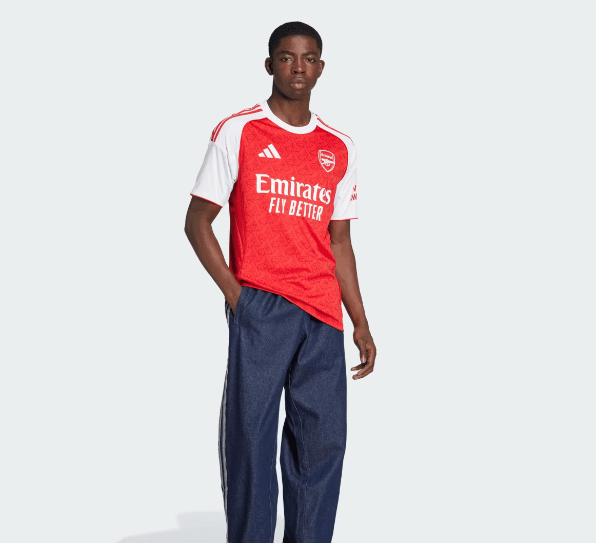 Screenshot2025-06-04184943 | AE JERSEY Man modeling an Arsenal football jersey (red with white sleeves) paired with dark blue jeans, posing confidently against a light background.