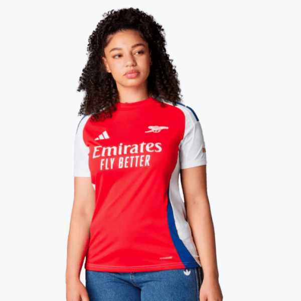 Female model wearing Arsenal away jersey: red body, white sleeves, blue side panels, Emirates Fly Better logo.