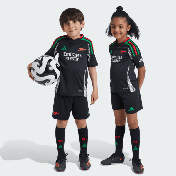 Two children in black Arsenal youth soccer kits stand side by side, one holding a soccer ball against a light background.