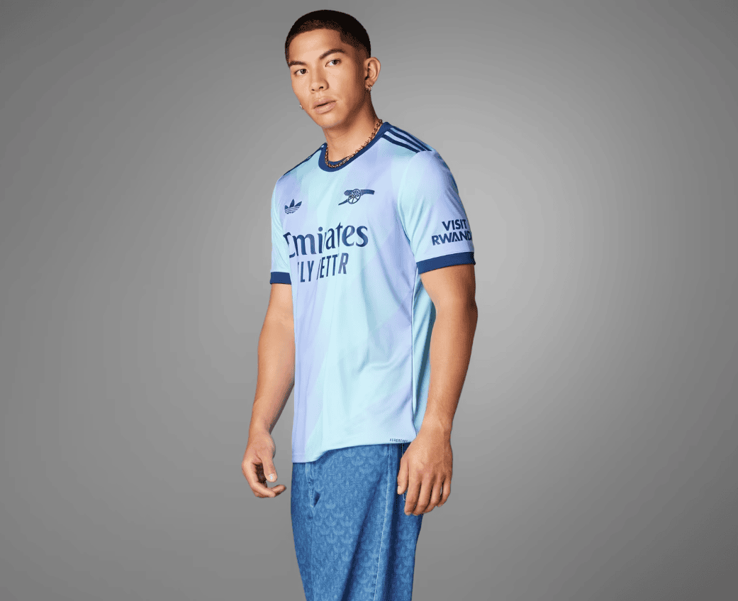 Screenshot_2024-09-18_194428_3d551ac5-a7f2-4e14-a0a8-43cb49f4f38f | AE JERSEY Man wearing a light blue Real Madrid jersey, standing in a neutral gray studio backdrop, facing slightly to the right.