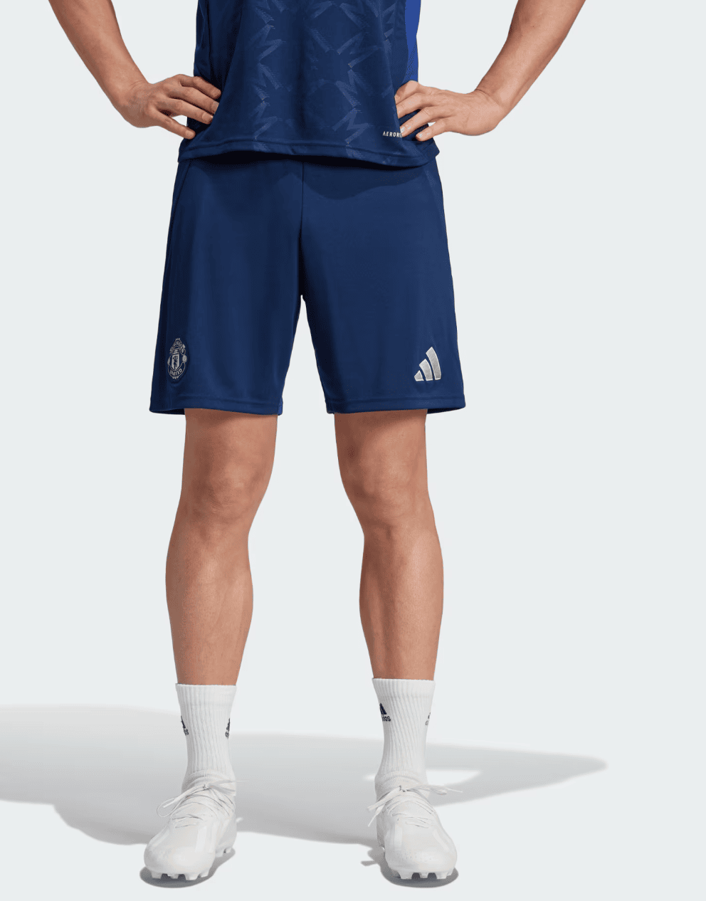 Screenshot_2024-09-18_222513 | AE JERSEY Person shown from the waist down wearing navy blue soccer shorts with a club badge on the left leg and a logo on the right; white crew socks and white cleats are visible, standing with hands on hips.