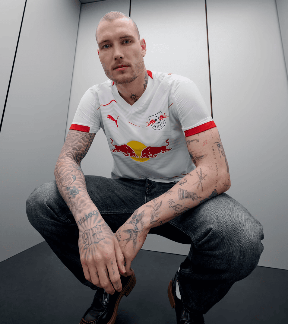 Screenshot_2025-06-19_045228 | AE JERSEY Crouching man with a shaved head and tattoos in a white RB Leipzig jersey, standing in an elevator and looking at the camera.