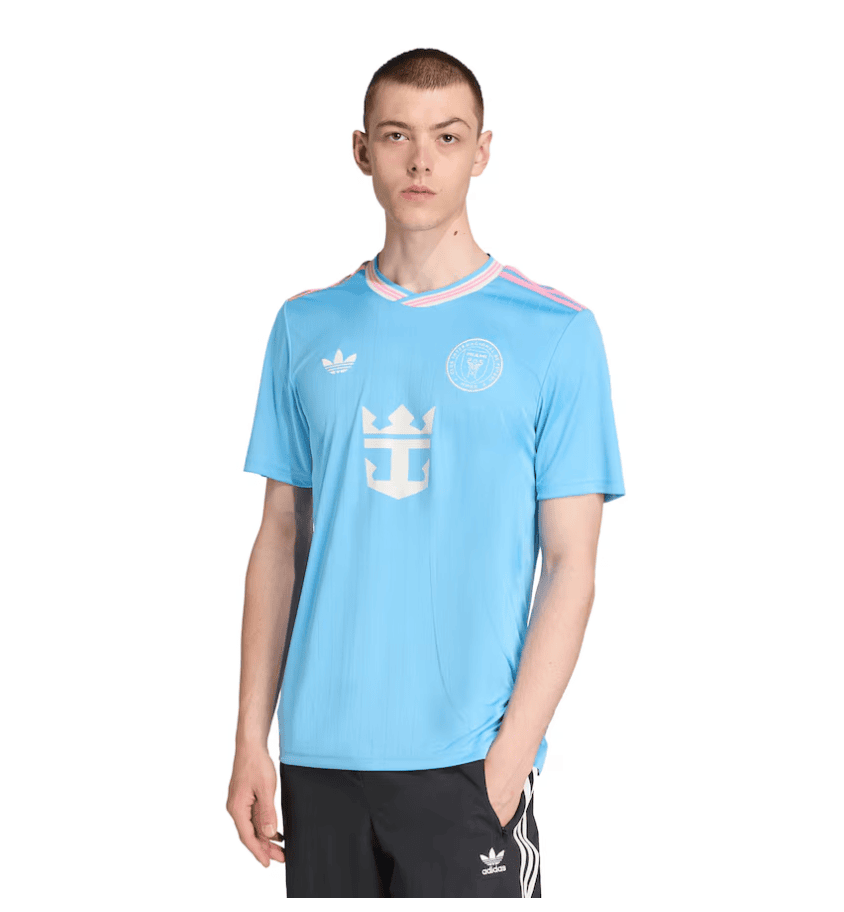 Screenshot_2025-06-23_181518 | AE JERSEY Young male model wearing a sky-blue Adidas soccer jersey with a white crest and pink-trim collar, standing against a white background.
