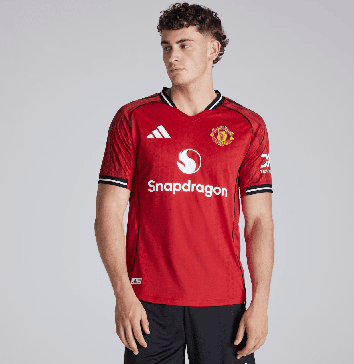 Screenshot_2025-06-25_061540 | AE JERSEY Male model wearing a red Manchester United football jersey with Snapdragon logo and club crest on the chest, facing left.