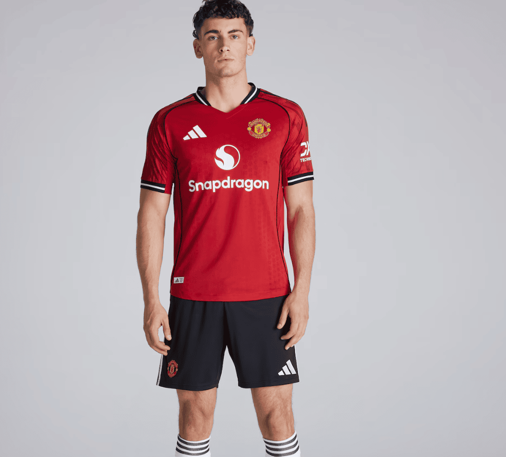 Screenshot_2025-06-25_061553 | AE JERSEY Man wearing a red Manchester United jersey with Snapdragon sponsor, black shorts, and striped socks, posing for a product shot.