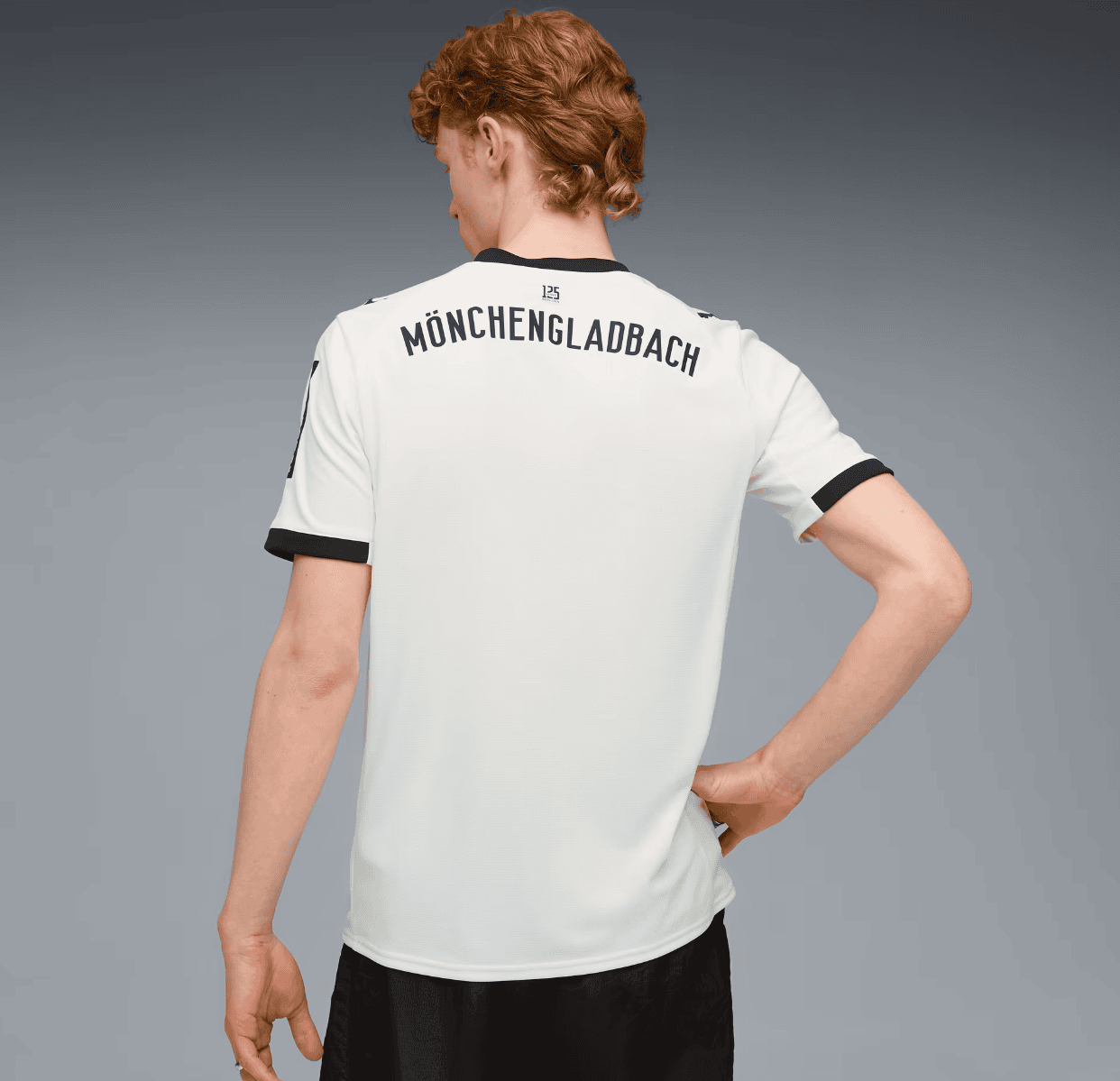 Screenshot_2025-07-16_205624 | AE JERSEY Back view of a person wearing a white soccer jersey with 'MÖNCHENGLADBACH' printed across the top, black collar and sleeve trim, against a gray gradient background.