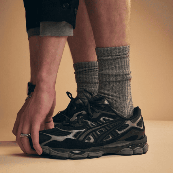Person tying the laces of a dark athletic sneaker while wearing thick gray socks.