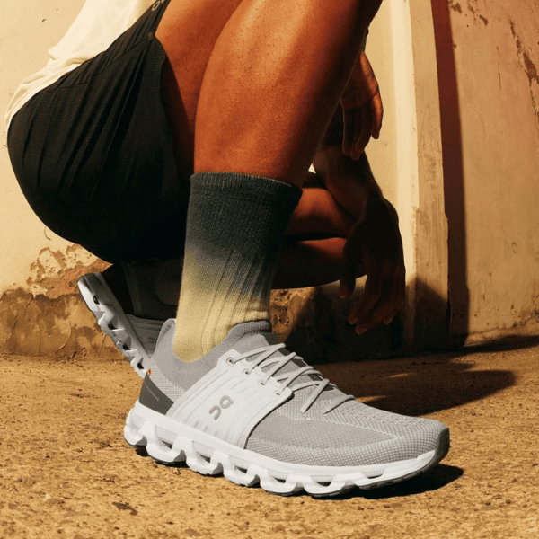 Person crouching on a sunlit concrete surface, wearing gray running shoes and olive-green socks.